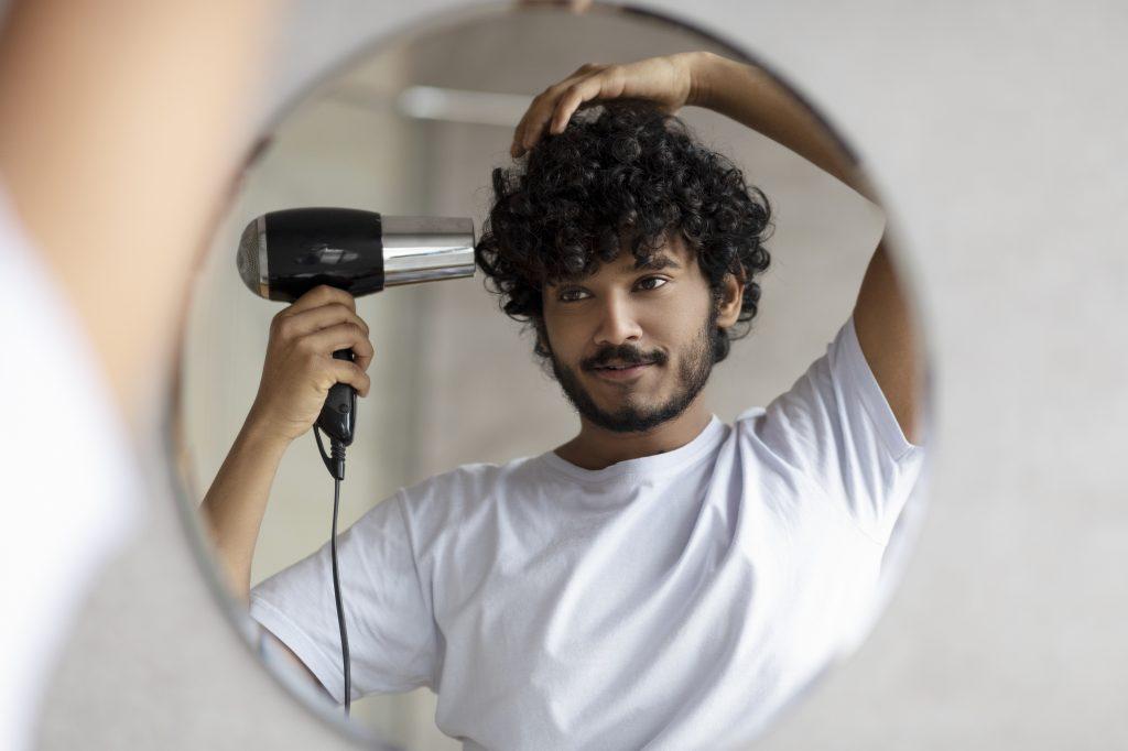Bel homme séchant ses cheveux après la douche, se coiffant, prenant soin de lui le matin, regardant son reflet dans le miroir. Concept d'hygiène quotidienne